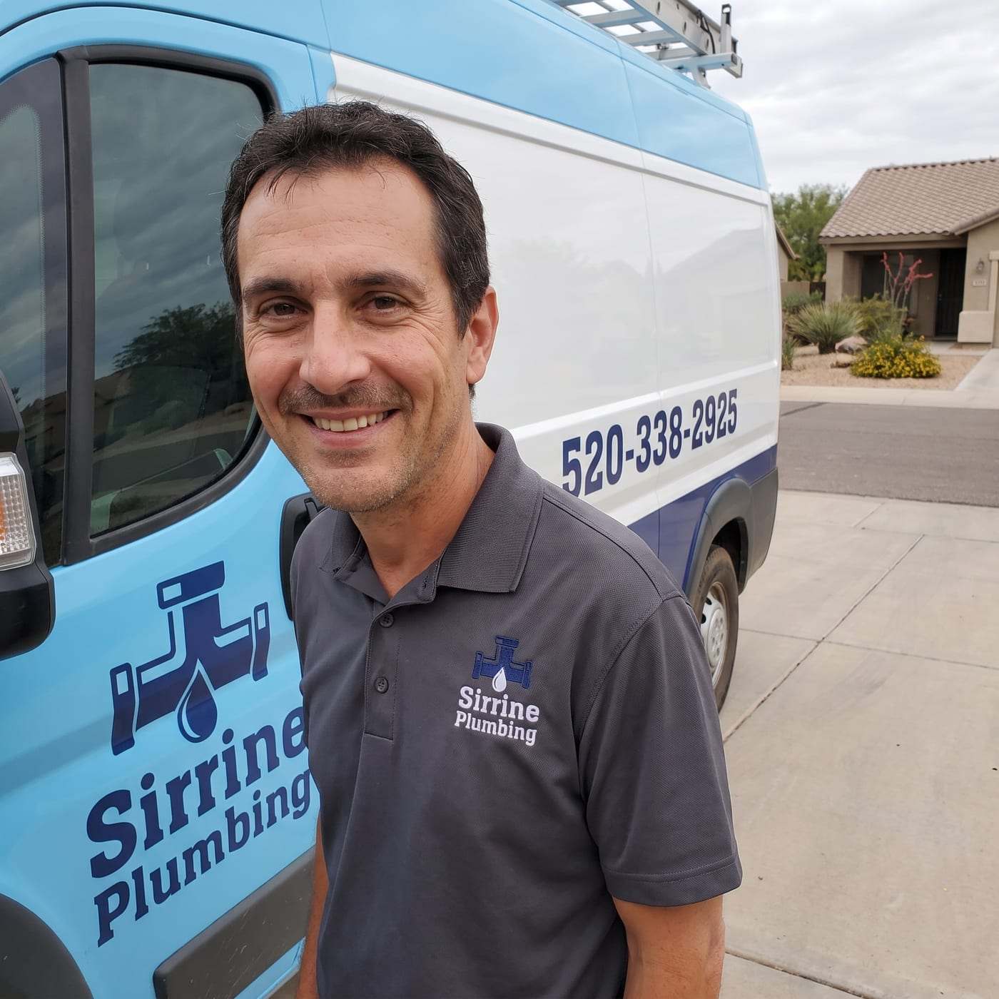Jayden Burns in a charcoal Sirrine Plumbing polo, smiling beside the company van at a curb