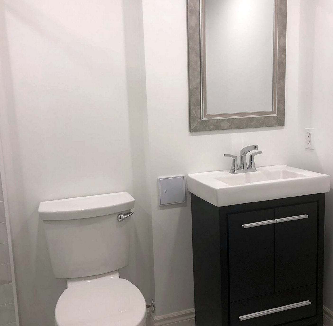 Finished half bath with a white toilet, a dark vanity with a chrome faucet and a framed mirror