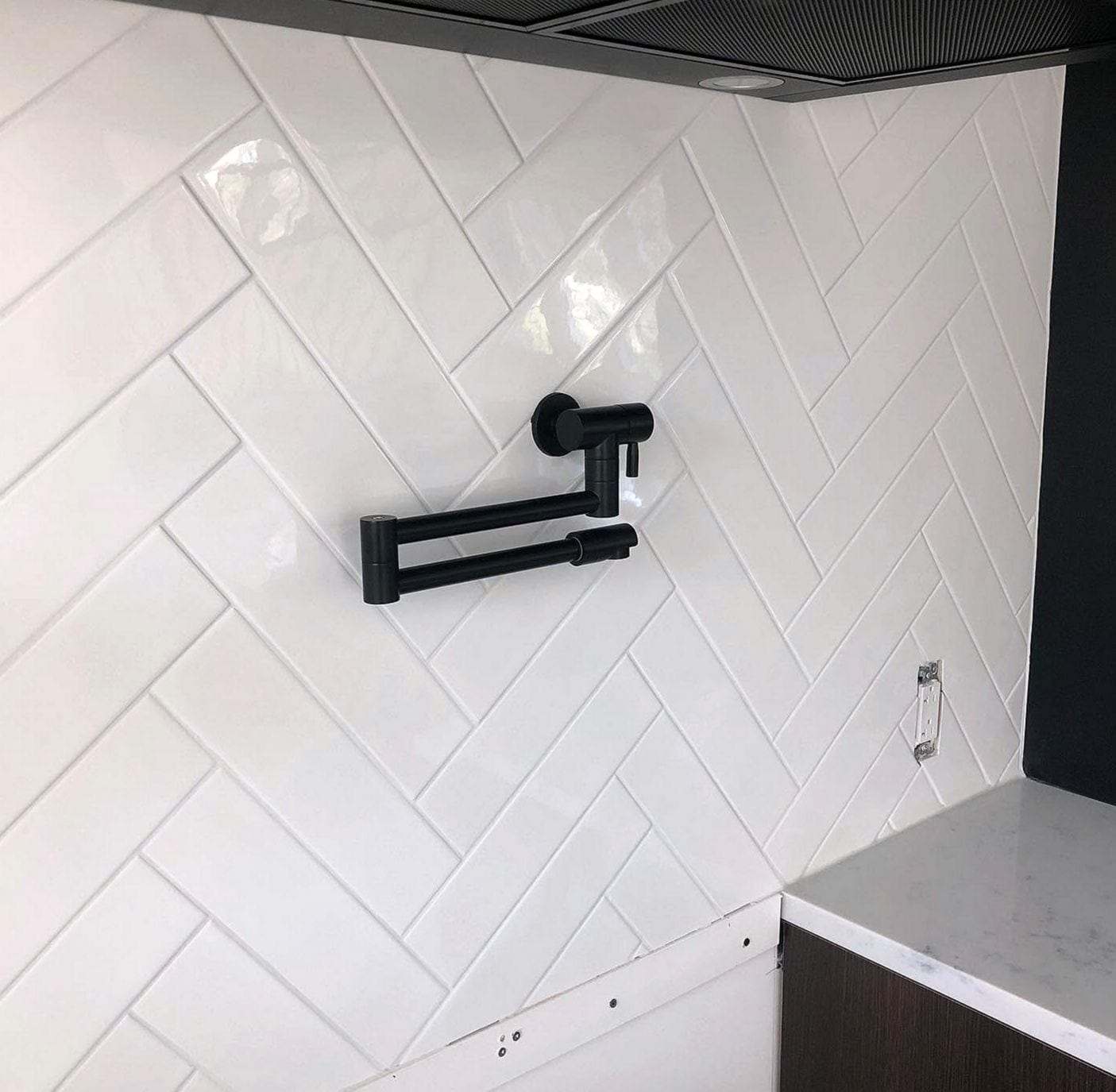 Black wall-mounted pot filler faucet folded against white herringbone tile