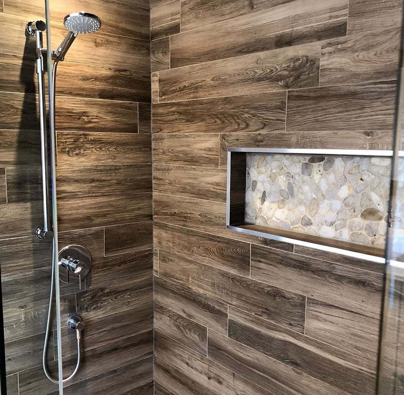 Walk-in shower with wood-look tile, a chrome slide-bar hand shower and a recessed niche lined with pebbles