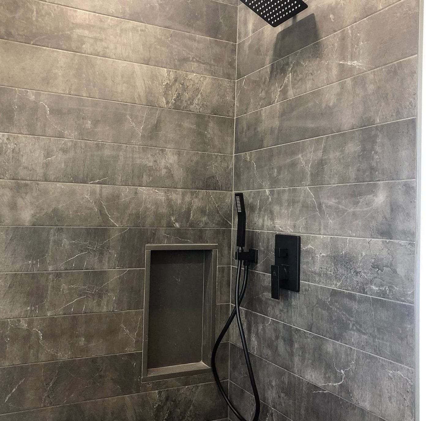 Gray stone-look tile shower with a square rain head, a black hand shower and a black valve trim plate